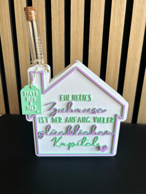 3D-gedruckter Hausaufsteller in Weiß, Mint und Lila mit Reagenzglas und Spruch „Ein neues Zuhause ist der Anfang vieler glücklicher Kapitel"
